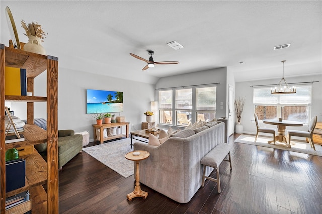 living room featuring ceiling fan with notable chandelier, dark wood-type flooring, and vaulted ceiling