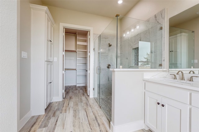 full bath featuring recessed lighting, wood finished floors, vanity, a marble finish shower, and a walk in closet