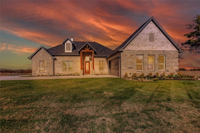 french country style house featuring a chimney, an attached garage, stone siding, driveway, and a front lawn