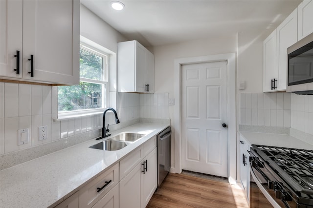 kitchen with stainless steel appliances, sink, light stone countertops, light wood-type flooring, and white cabinetry