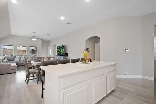 kitchen with a kitchen island, a kitchen breakfast bar, light hardwood / wood-style flooring, vaulted ceiling, and white cabinetry