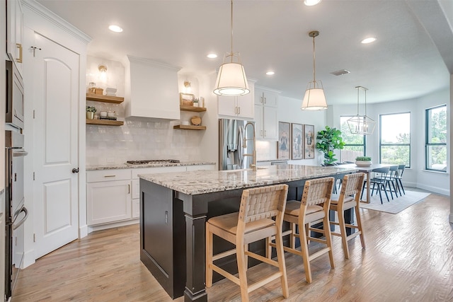 kitchen with light hardwood / wood-style floors, pendant lighting, a center island with sink, and white cabinets