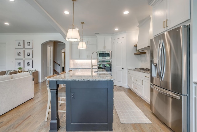 kitchen featuring a kitchen island with sink, white cabinetry, decorative light fixtures, and stainless steel appliances