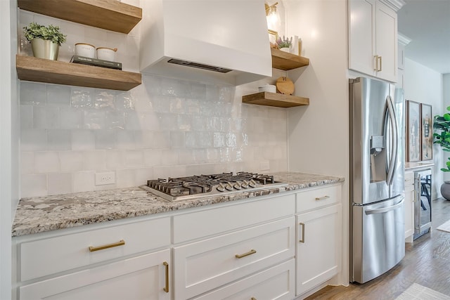 kitchen featuring backsplash, appliances with stainless steel finishes, extractor fan, white cabinetry, and light wood-type flooring