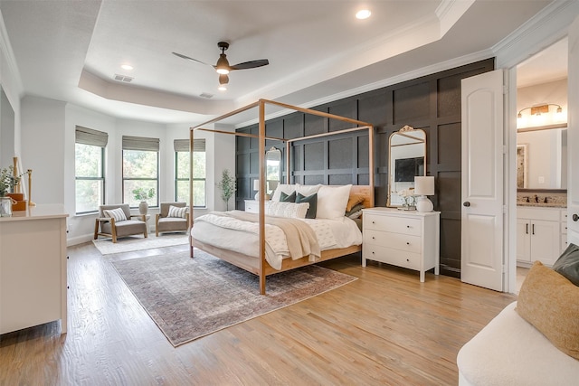 bedroom with light hardwood / wood-style floors, ceiling fan, ensuite bath, and a raised ceiling