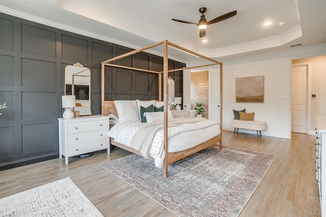 bedroom featuring crown molding, light hardwood / wood-style flooring, a tray ceiling, and ceiling fan