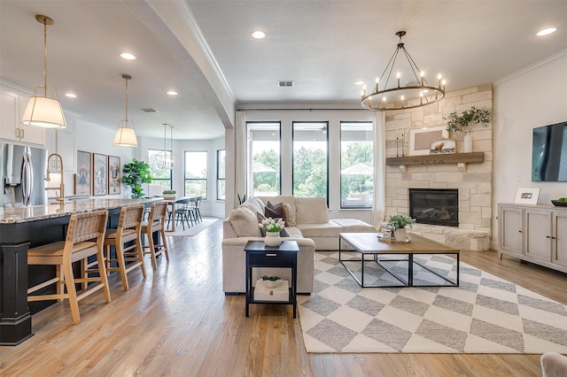 living room featuring crown molding, a stone fireplace, light hardwood / wood-style flooring, and a chandelier