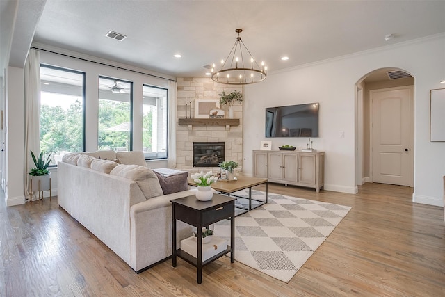 living room featuring crown molding, a stone fireplace, light hardwood / wood-style flooring, and an inviting chandelier