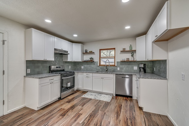 kitchen with light stone counters, appliances with stainless steel finishes, dark hardwood / wood-style floors, sink, and white cabinets