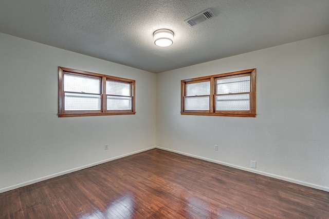 spare room featuring dark wood-type flooring, a healthy amount of sunlight, and a textured ceiling