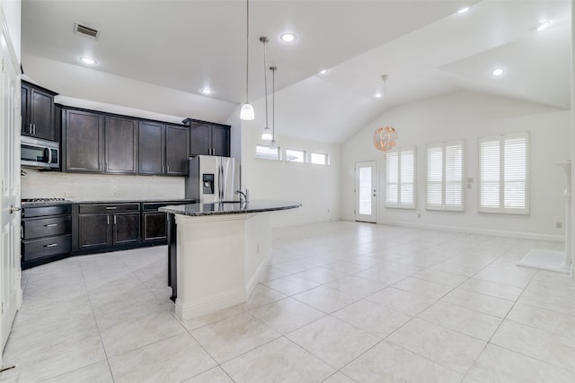 kitchen featuring appliances with stainless steel finishes, vaulted ceiling, dark stone countertops, decorative backsplash, and a kitchen island with sink