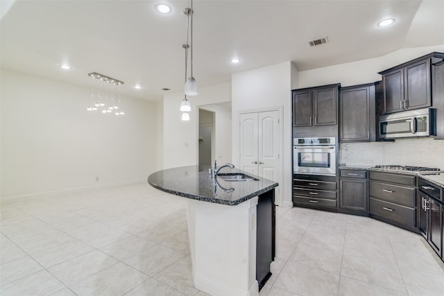 kitchen featuring appliances with stainless steel finishes, sink, dark stone counters, pendant lighting, and a kitchen island with sink