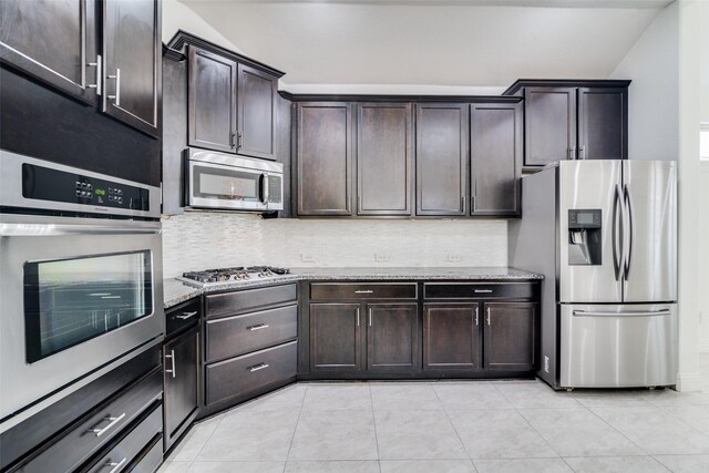 kitchen featuring stainless steel appliances, backsplash, light stone counters, and dark brown cabinetry