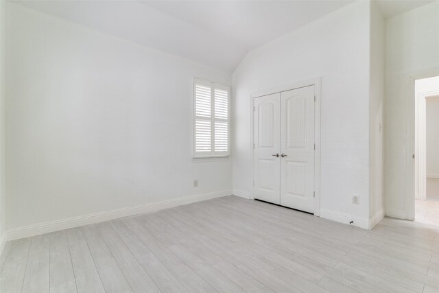 unfurnished bedroom with light wood-style floors, vaulted ceiling, baseboards, and a closet