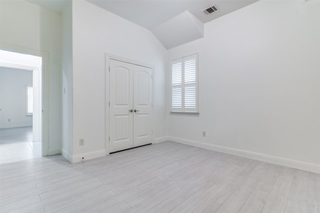 unfurnished bedroom featuring lofted ceiling, a closet, and light wood-type flooring