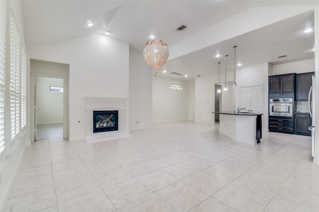 unfurnished living room featuring a chandelier, lofted ceiling, light tile patterned floors, a glass covered fireplace, and recessed lighting