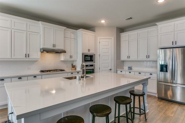 kitchen featuring white cabinets, tasteful backsplash, a kitchen island with sink, light hardwood / wood-style flooring, and stainless steel appliances