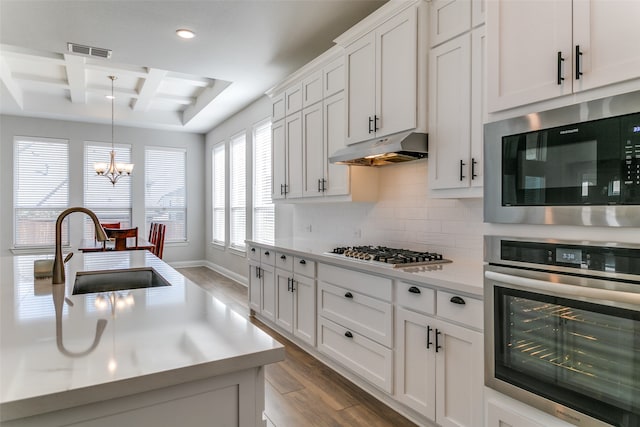 kitchen with beamed ceiling, stainless steel appliances, hardwood / wood-style floors, sink, and decorative light fixtures