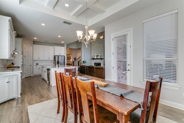 dining space with light hardwood / wood-style flooring, beam ceiling, a chandelier, and sink