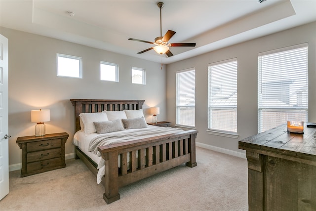 carpeted bedroom with multiple windows, a tray ceiling, and ceiling fan