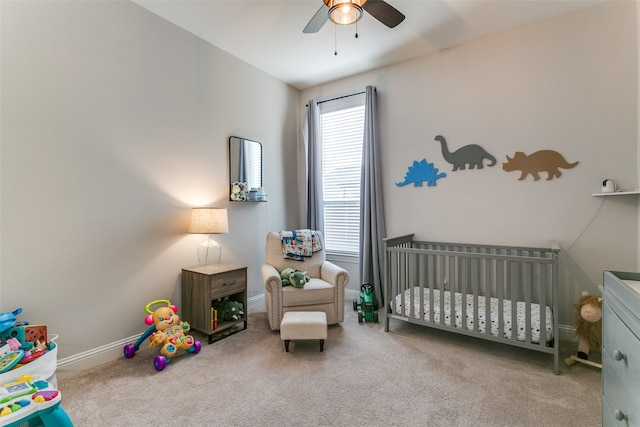 carpeted bedroom featuring ceiling fan and a nursery area