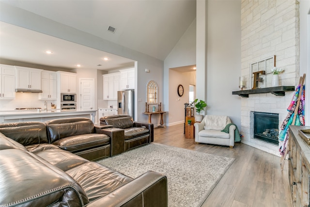 living room featuring a stone fireplace, light hardwood / wood-style flooring, high vaulted ceiling, and sink