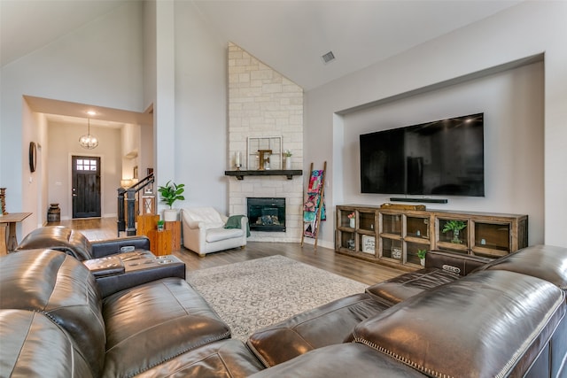 living room with a notable chandelier, a stone fireplace, hardwood / wood-style flooring, and high vaulted ceiling