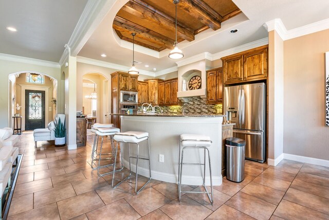 kitchen with decorative backsplash, a kitchen island with sink, a breakfast bar area, hanging light fixtures, and stainless steel appliances