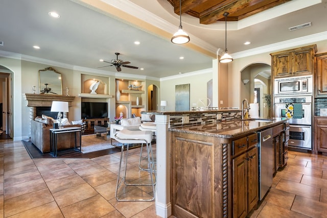 kitchen with hanging light fixtures, a center island with sink, a kitchen breakfast bar, ornamental molding, and sink