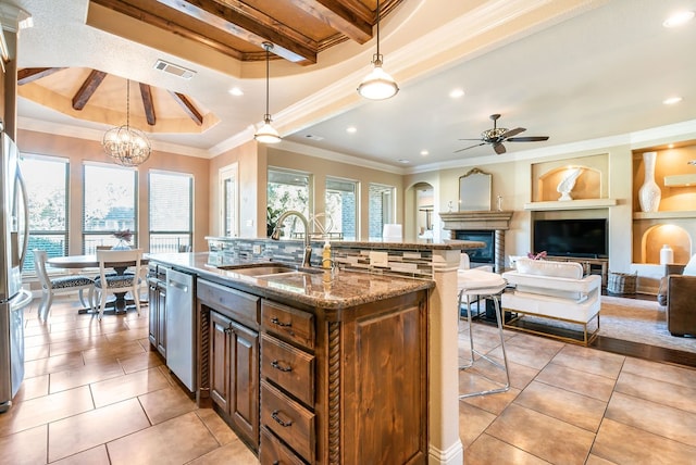 kitchen featuring hanging light fixtures, stainless steel appliances, beamed ceiling, crown molding, and a kitchen island with sink