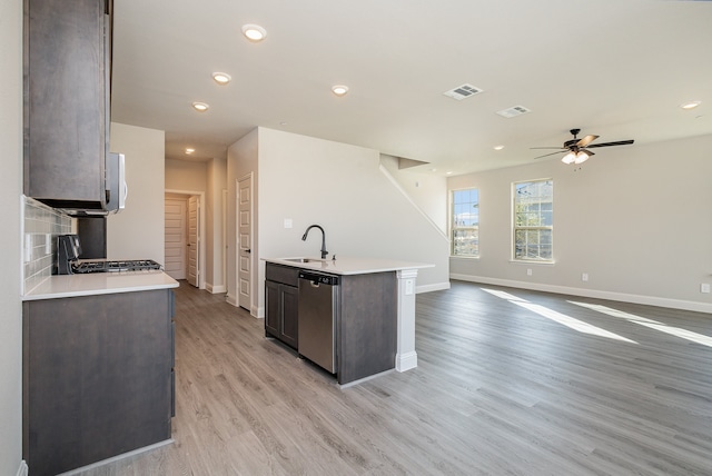 kitchen with a kitchen island with sink, light hardwood / wood-style flooring, sink, appliances with stainless steel finishes, and tasteful backsplash