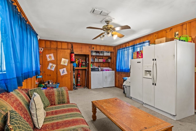 carpeted living room featuring ceiling fan, separate washer and dryer, and wood walls