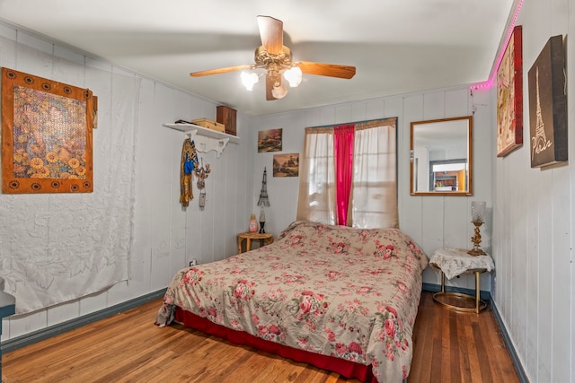 bedroom with dark hardwood / wood-style flooring, wooden walls, and ceiling fan