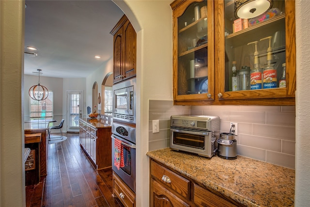 kitchen with dark wood-type flooring, hanging light fixtures, stainless steel appliances, light stone countertops, and a notable chandelier