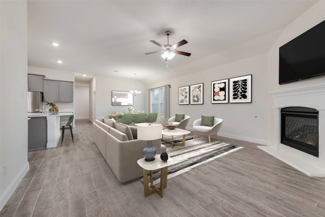 living room featuring ceiling fan with notable chandelier and light wood-type flooring