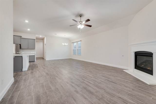 unfurnished living room with light wood-type flooring and ceiling fan with notable chandelier