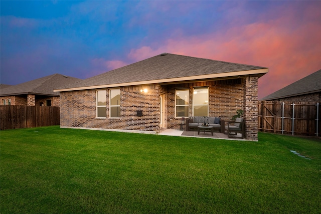 back house at dusk featuring a patio, an outdoor living space, and a lawn