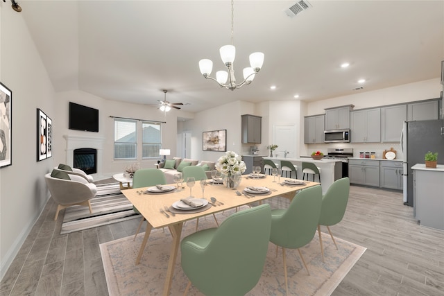 dining space with ceiling fan with notable chandelier and light wood-type flooring