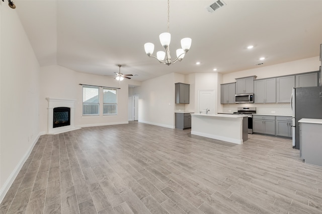 kitchen with appliances with stainless steel finishes, hanging light fixtures, light hardwood / wood-style floors, gray cabinets, and a center island with sink