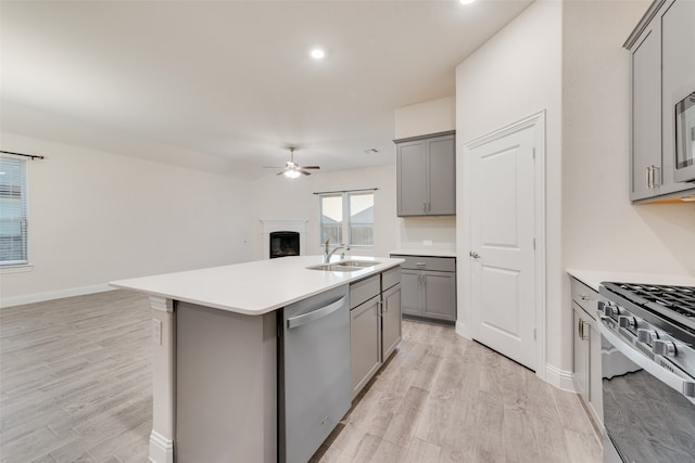 kitchen featuring light wood-type flooring, stainless steel appliances, sink, and an island with sink