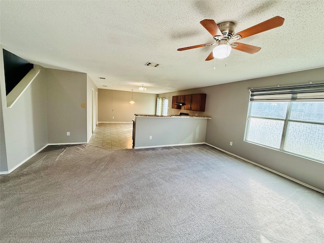 unfurnished living room featuring ceiling fan, light colored carpet, and a textured ceiling