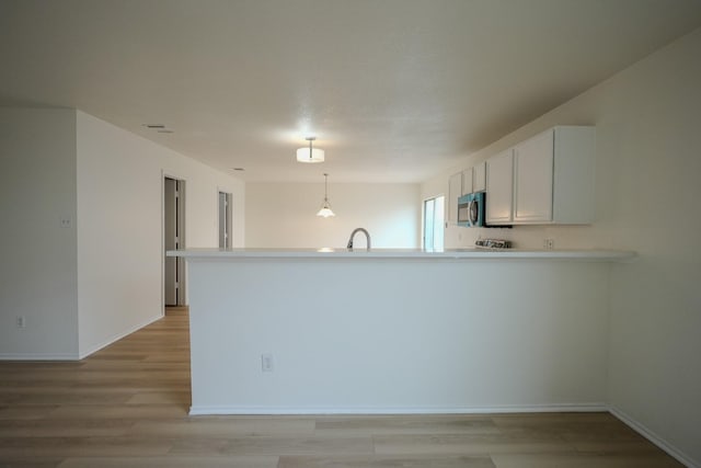 kitchen with stainless steel microwave, light wood-type flooring, a peninsula, white cabinets, and a sink