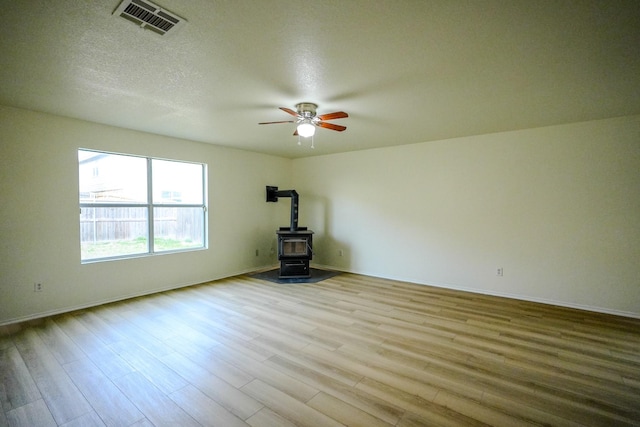 unfurnished room featuring visible vents, a wood stove, wood finished floors, a textured ceiling, and a ceiling fan