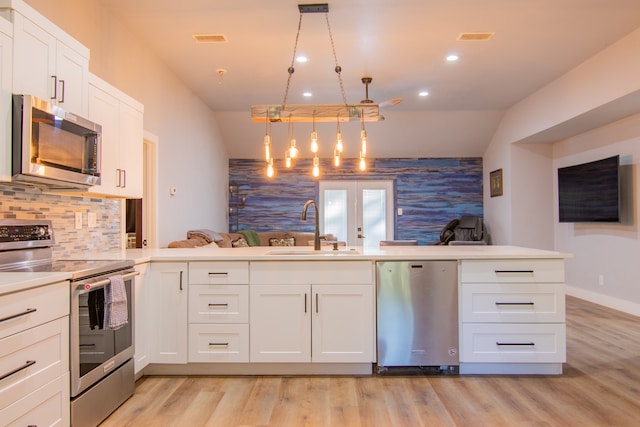 kitchen featuring kitchen peninsula, hanging light fixtures, white cabinetry, sink, and stainless steel appliances