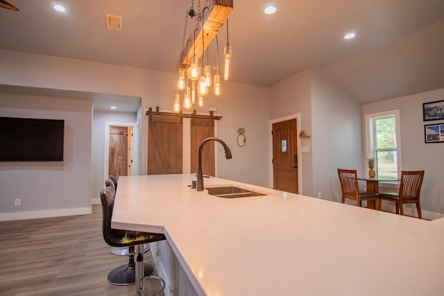 kitchen featuring wood-type flooring, sink, a barn door, vaulted ceiling, and pendant lighting