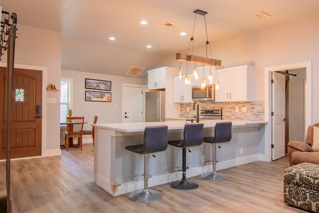 kitchen featuring lofted ceiling, stainless steel appliances, pendant lighting, light wood-type flooring, and white cabinetry