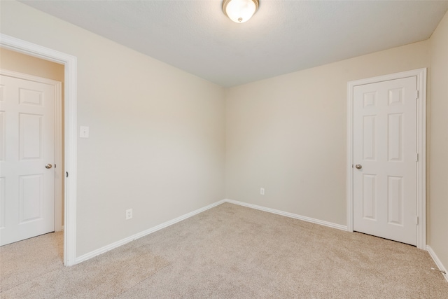 spare room with baseboards and light colored carpet