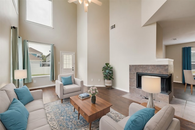 living room with hardwood / wood-style floors, a high ceiling, a tile fireplace, and ceiling fan