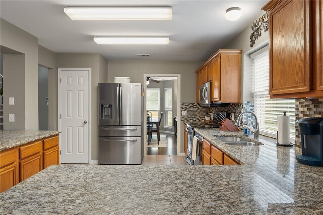 628 Destin Dr, Fort Worth, TX 76131 - kitchen featuring appliances with stainless steel finishes, a sink, brown cabinetry, and tasteful backsplash