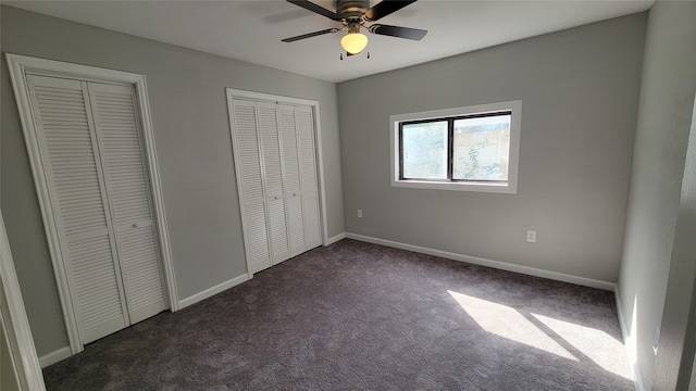 unfurnished bedroom featuring multiple closets, dark carpet, and ceiling fan